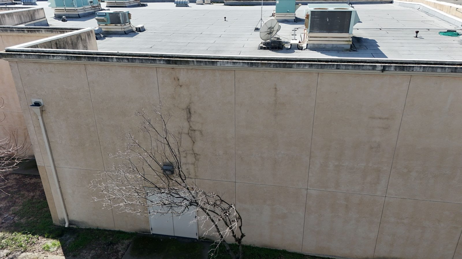 Aerial view of a commercial building's rooftop equipment and exterior wall showing vertical staining and cracking running down from the parapet