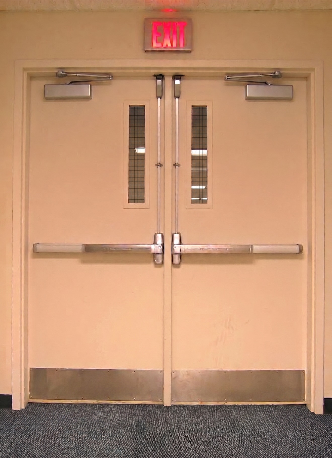 Pair of labeled fire-rated exit doors with door closers, vision lites, and panic bar hardware, below a lit EXIT sign